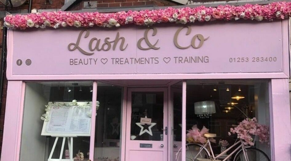 Charming pink storefront of Lash & Co in Fleetwood, England, GB, adorned with flowers and vintage bicycle.