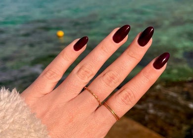 Elegant crimson manicured nails by Beau Nails, San Ġwann, MT, showcased against a serene water backdrop.