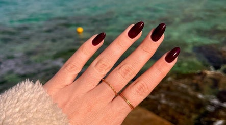 Elegant crimson manicured nails by Beau Nails, San Ġwann, MT, showcased against a serene water backdrop.