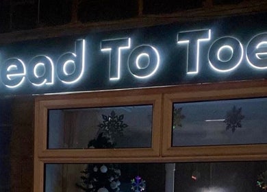 Illuminated 'Head to Toe' storefront sign at Grassmoor, England, GB, showcasing welcoming entrance.