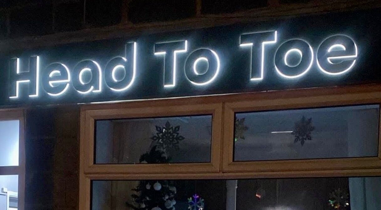 Illuminated 'Head to Toe' store sign at Grassmoor, England, GB showcasing the beauty and wellness venue.