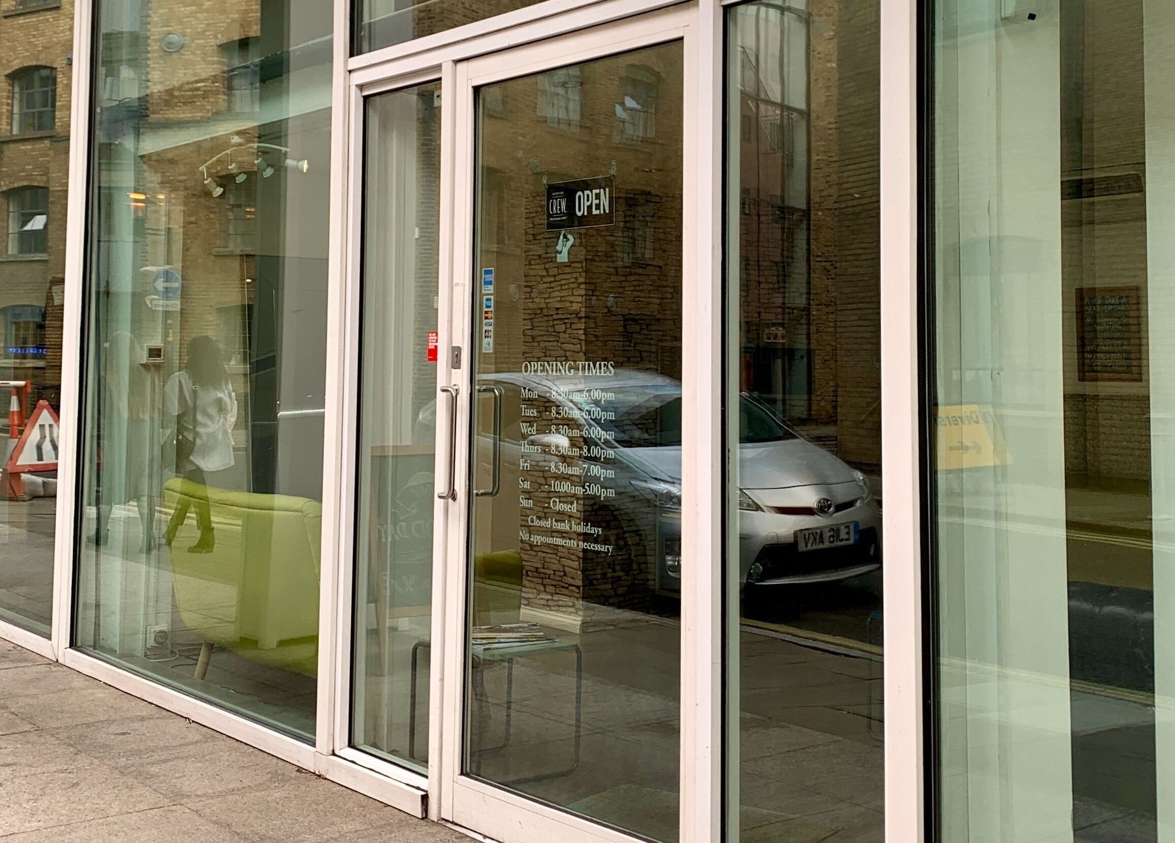Front glass entrance of Copper Row Barbers in London, England, GB showcasing opening hours.