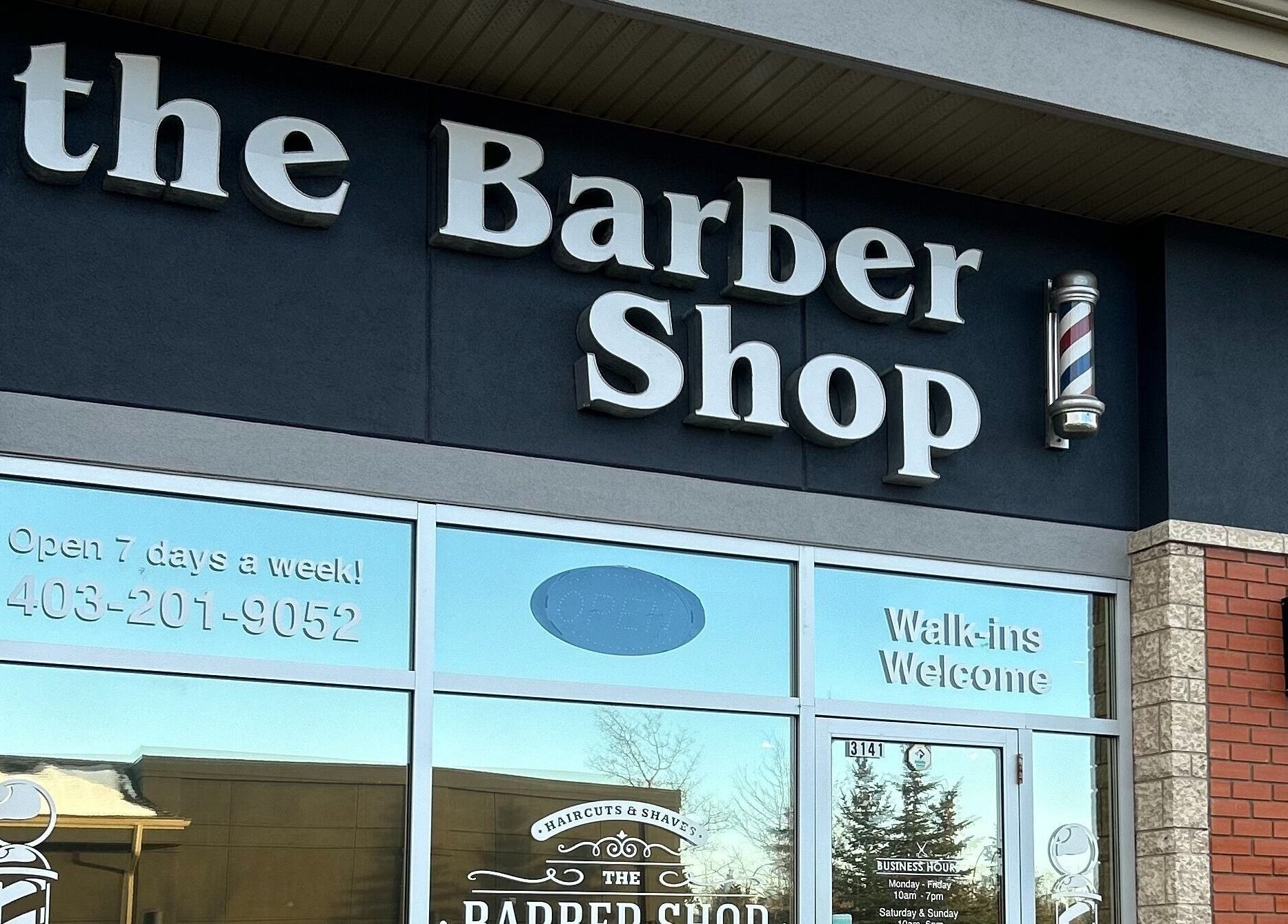 Exterior view of Brotherhood Barber Shop Millrise in Calgary, Alberta, CA with open sign and barber pole.