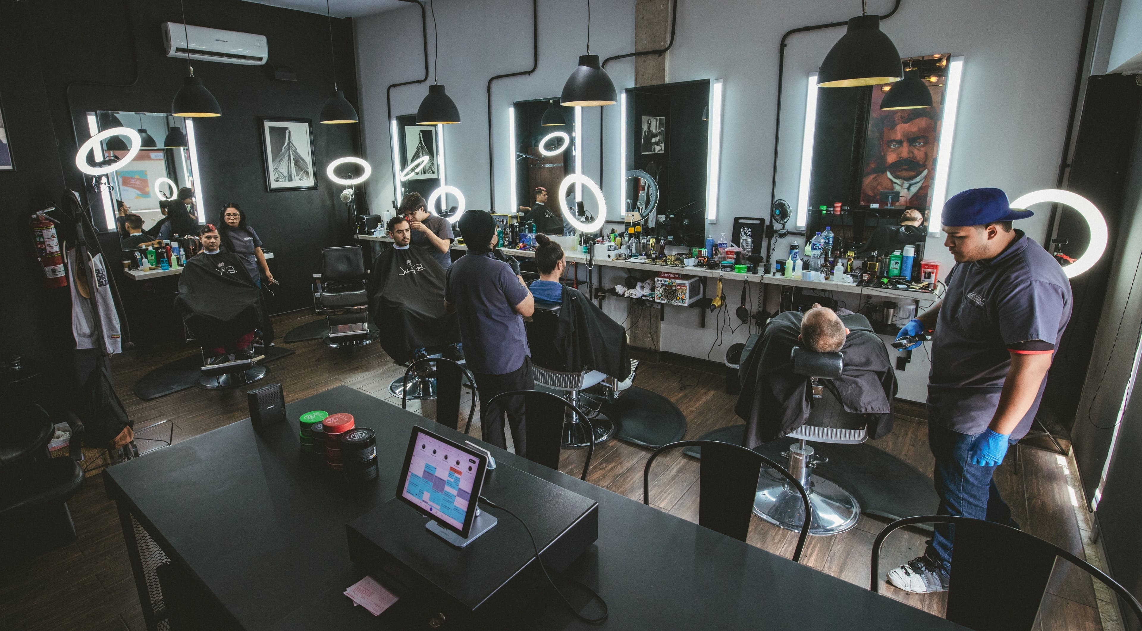 Modern barber shop interior at Barbería H, Tijuana, Baja California, MX with clients and barbers at work.