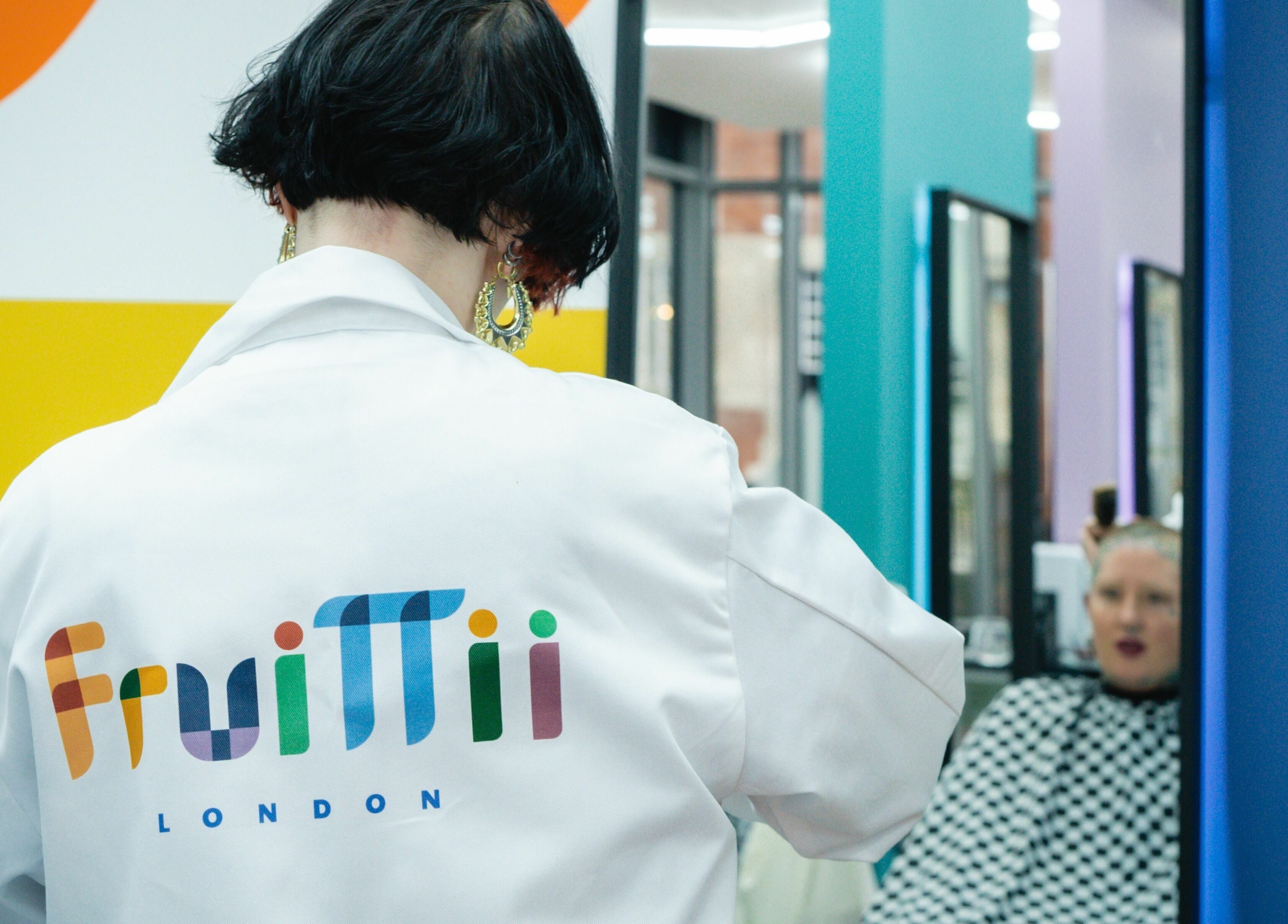 Stylist in Fruittii London coat at work in vibrant salon, London, England, GB.