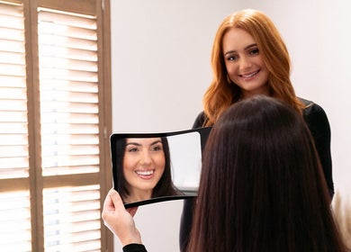 Client smiles at Charlotte Luxon Brow Stylist in Forres, Scotland, GB, holding a mirror reflecting her styled brows.