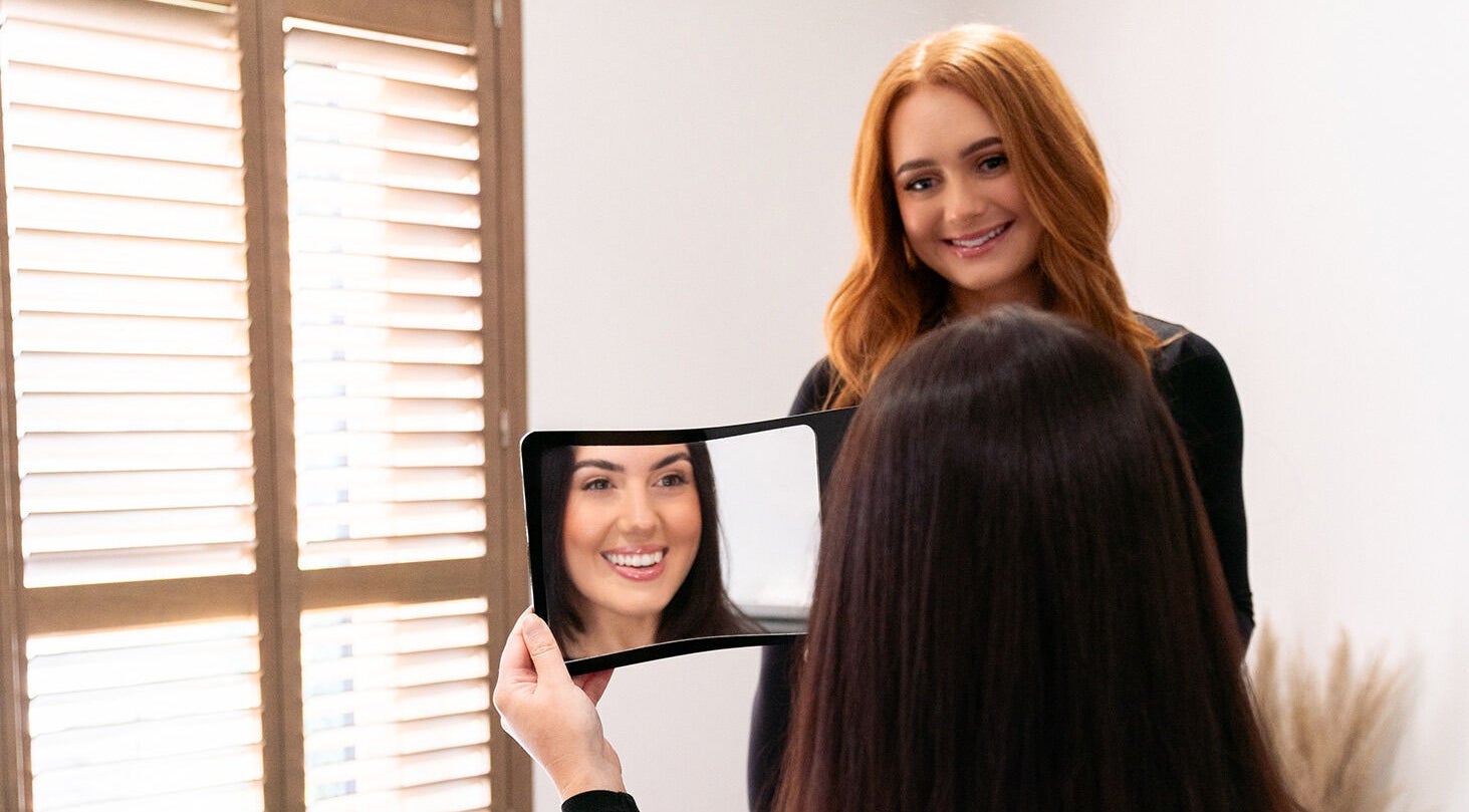 Client smiles at Charlotte Luxon Brow Stylist in Forres, Scotland, GB, holding a mirror reflecting her styled brows.
