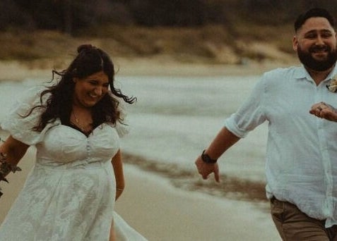 Couple in wedding attire happily runs on Corindi Beach near Labelleame Aesthetics, New South Wales, AU.
