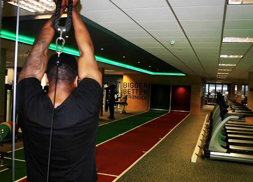 A gym-goer using equipment at Direct Gainz in Birmingham, England, GB, with treadmills and fitness area visible.