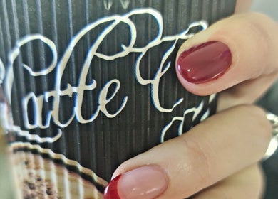 Stylish red-manicured nails holding a coffee cup at Royal Beauty in Bloemfontein, Free State, ZA.