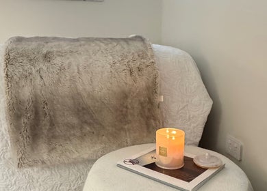 Cozy relaxation corner at Lash L'amour, Whangaparāoa, Auckland, NZ with a plush blanket and candle.