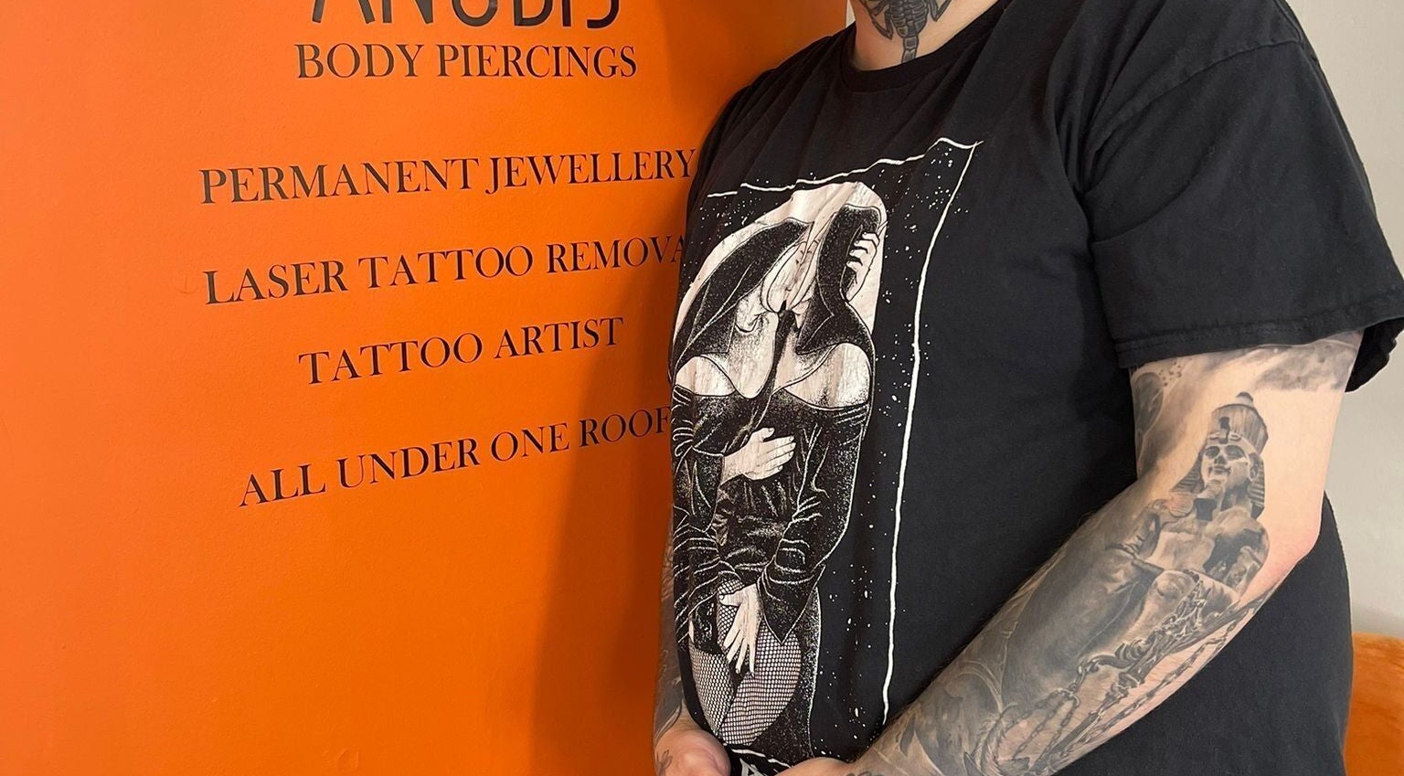 Tattooed person at Anubis Piercings and Laser Tattoo Removal, Ashby-de-la-zouch, England, with vibrant wall display.