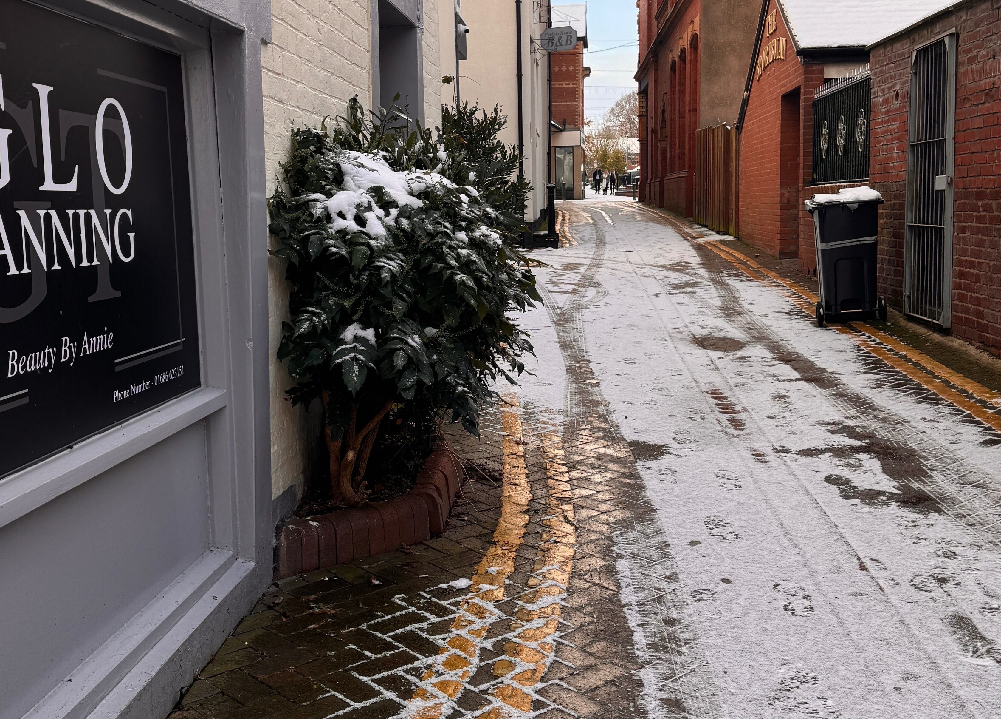 Glo Tanning & Beauty Salon Newtown sign on snow-covered path in Newtown, Wales, GB.