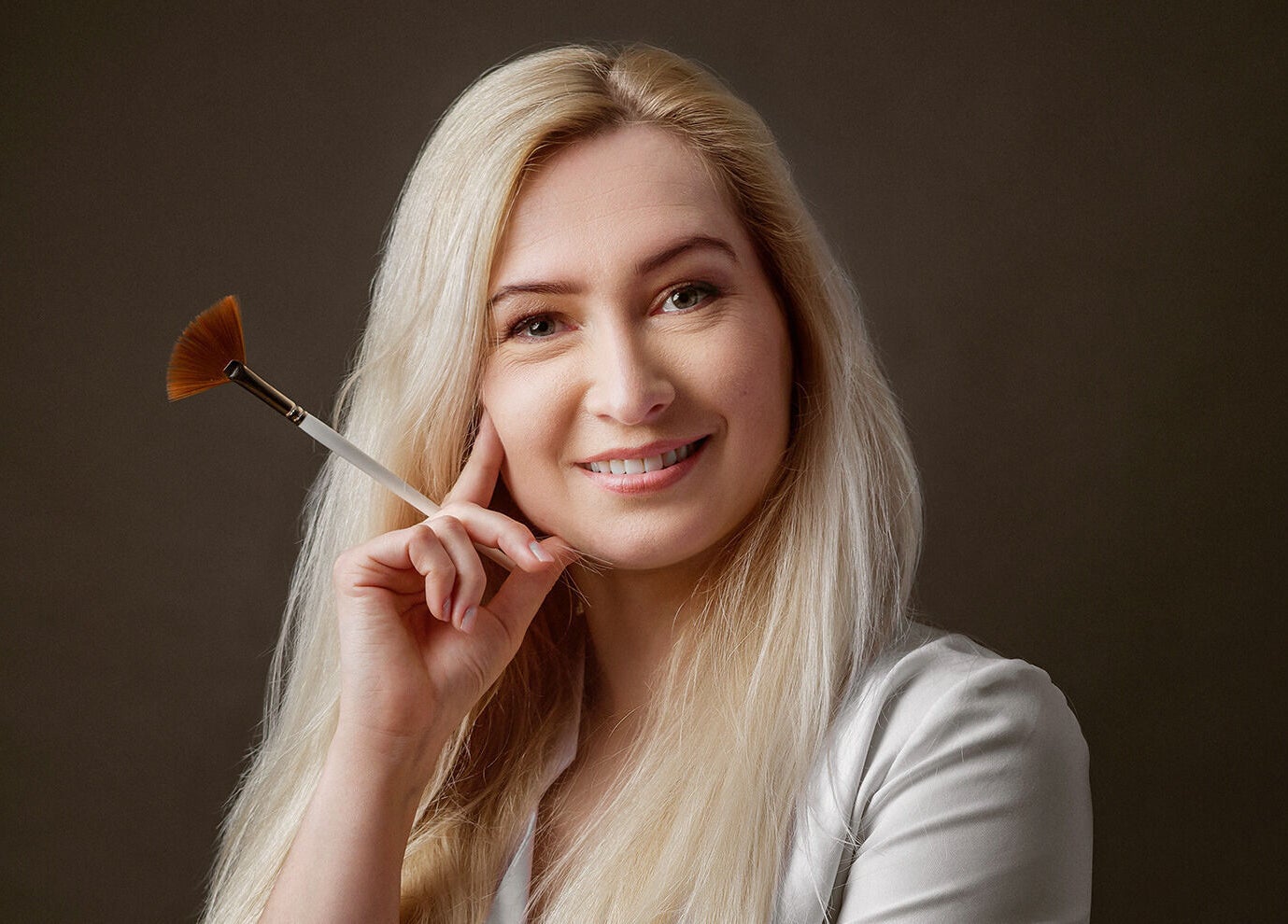 Professional beautician at Victoria Mac Skin, Carshalton, England, GB, holding a makeup brush and smiling.