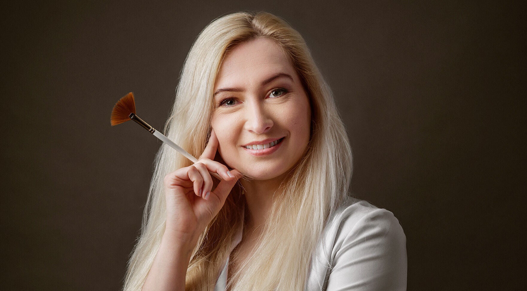 Professional beautician at Victoria Mac Skin, Carshalton, England, GB, holding a makeup brush and smiling.