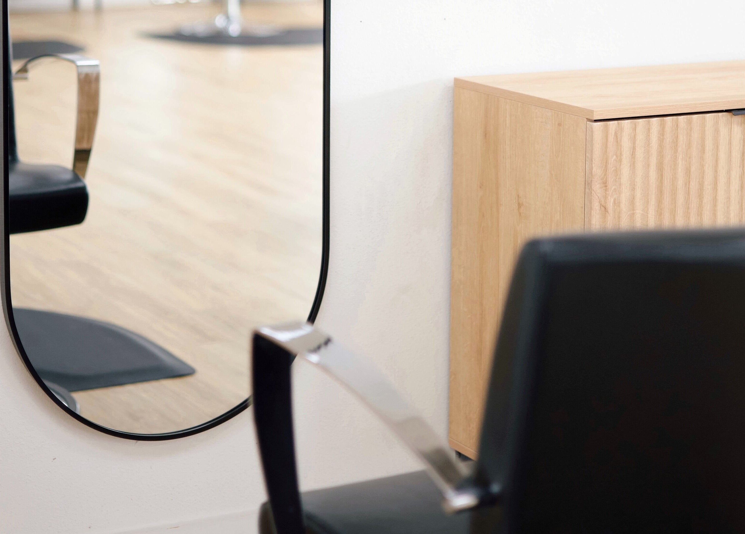 Elegant mirror in Sand + Sol Studio, Rogers, Arkansas, US showing a salon chair and wooden cabinet.