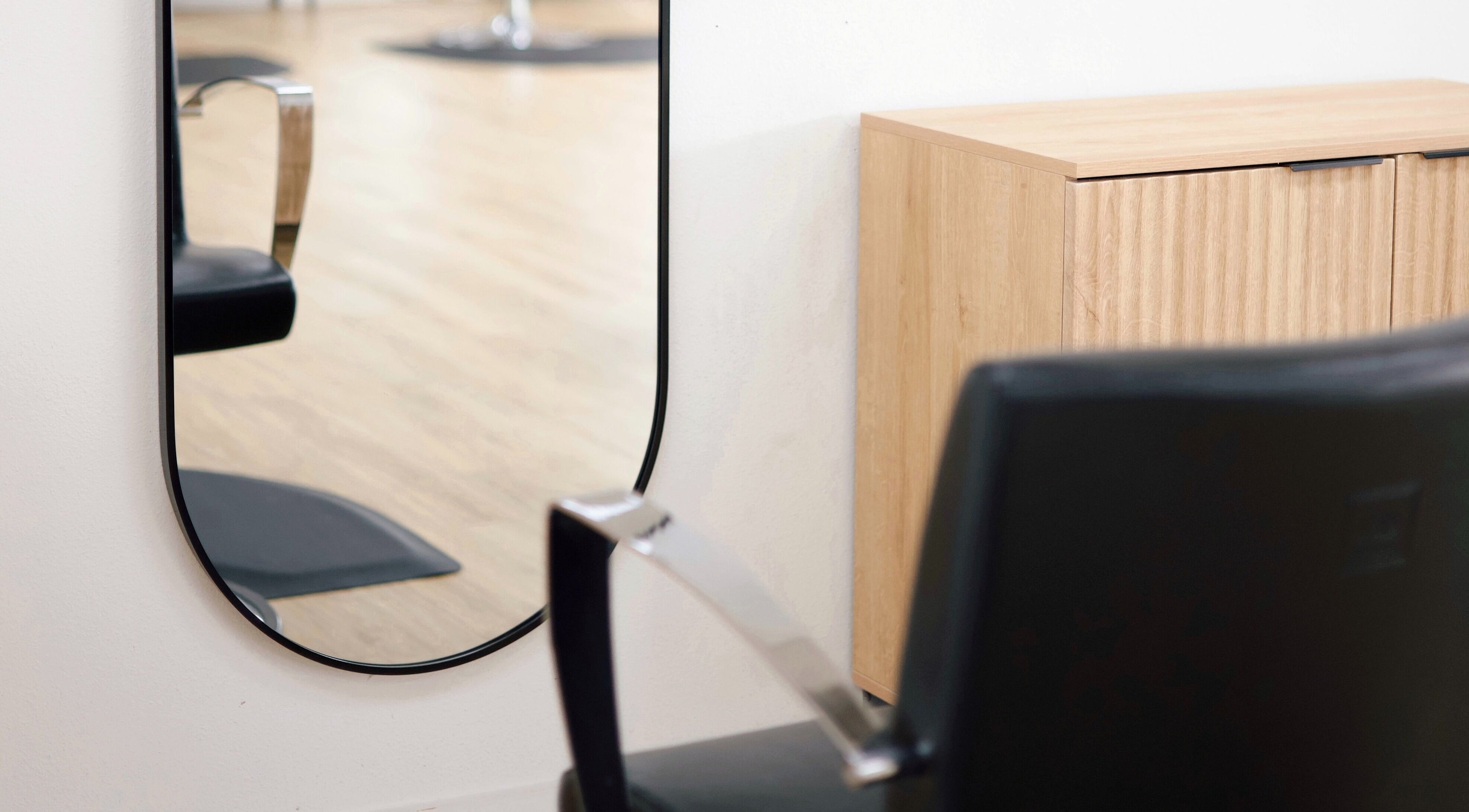 Elegant mirror in Sand + Sol Studio, Rogers, Arkansas, US showing a salon chair and wooden cabinet.