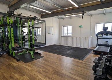 Modern gym area at Exe Fitness, Exmouth, England, GB, featuring weight racks and treadmill with ample lighting.