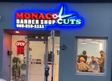 Monaco Cuts exterior in Hamilton, Ontario, CA, featuring a vibrant neon sign and barbers inside.