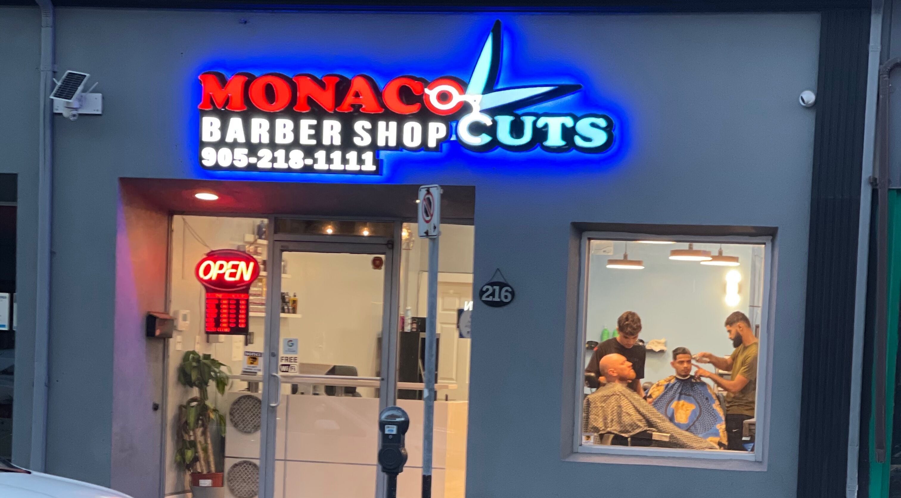 Monaco Cuts exterior in Hamilton, Ontario, CA, featuring a vibrant neon sign and barbers inside.