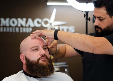 Barber at Monaco Cuts in Hamilton, Ontario, CA expertly trims a bearded man's hair.
