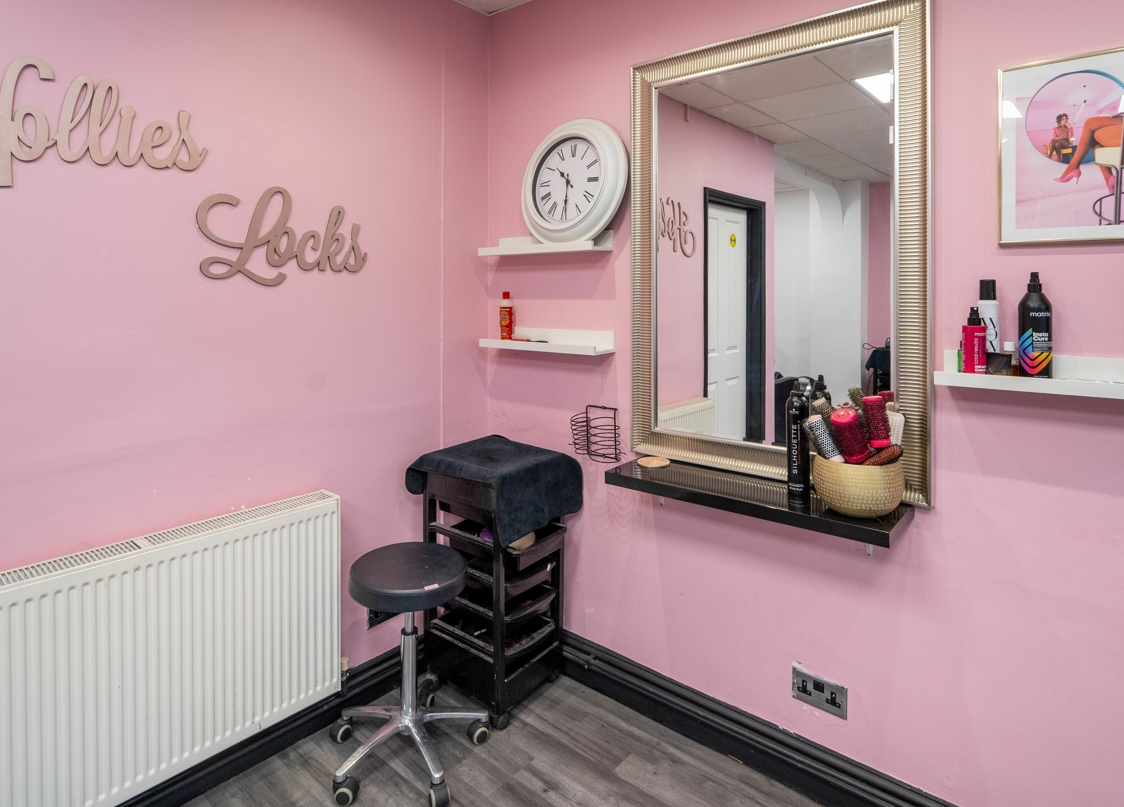 Inside Hollieslocks Salon in Hornchurch, England, GB featuring chic pink walls and a modern styling mirror.