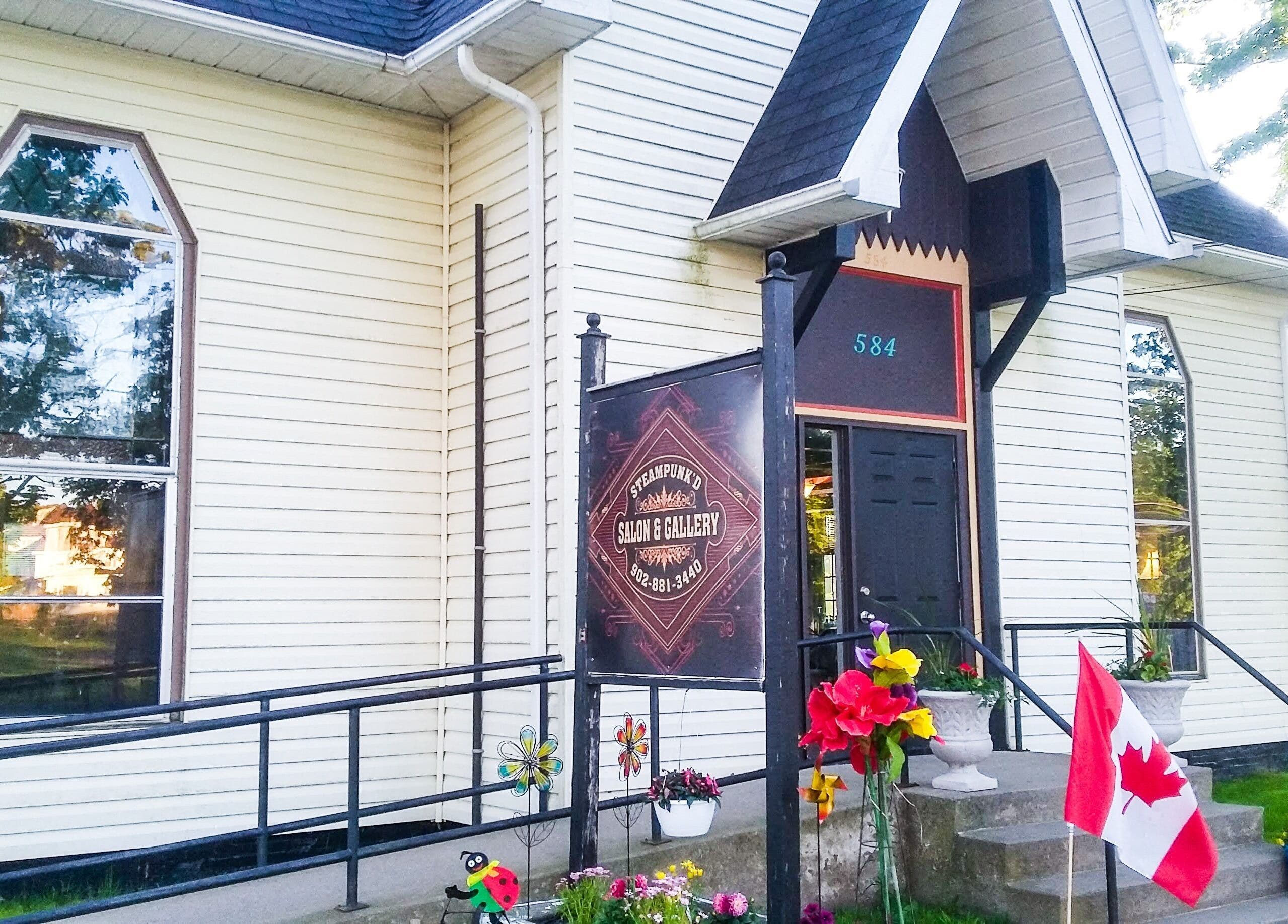 Front entrance of Steampunk'd Salon and Gallery, Yarmouth, Nova Scotia, CA, adorned with flags and flowers.