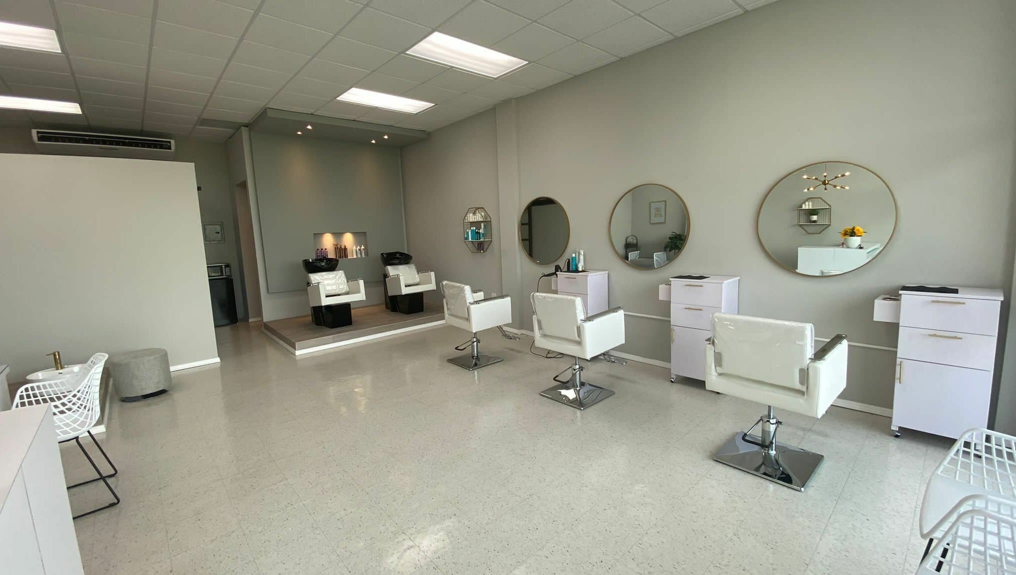 Interior moderno del Adara Hair Salón en Barceloneta, Barceloneta, PR, con sillas blancas y espejos circulares.