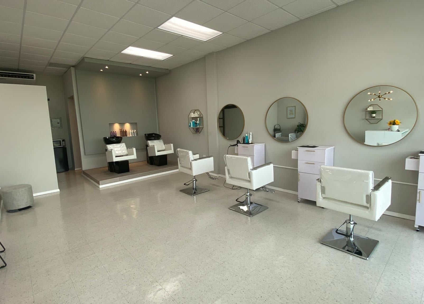 Interior moderno del Adara Hair Salón en Barceloneta, Barceloneta, PR, con sillas blancas y espejos circulares.