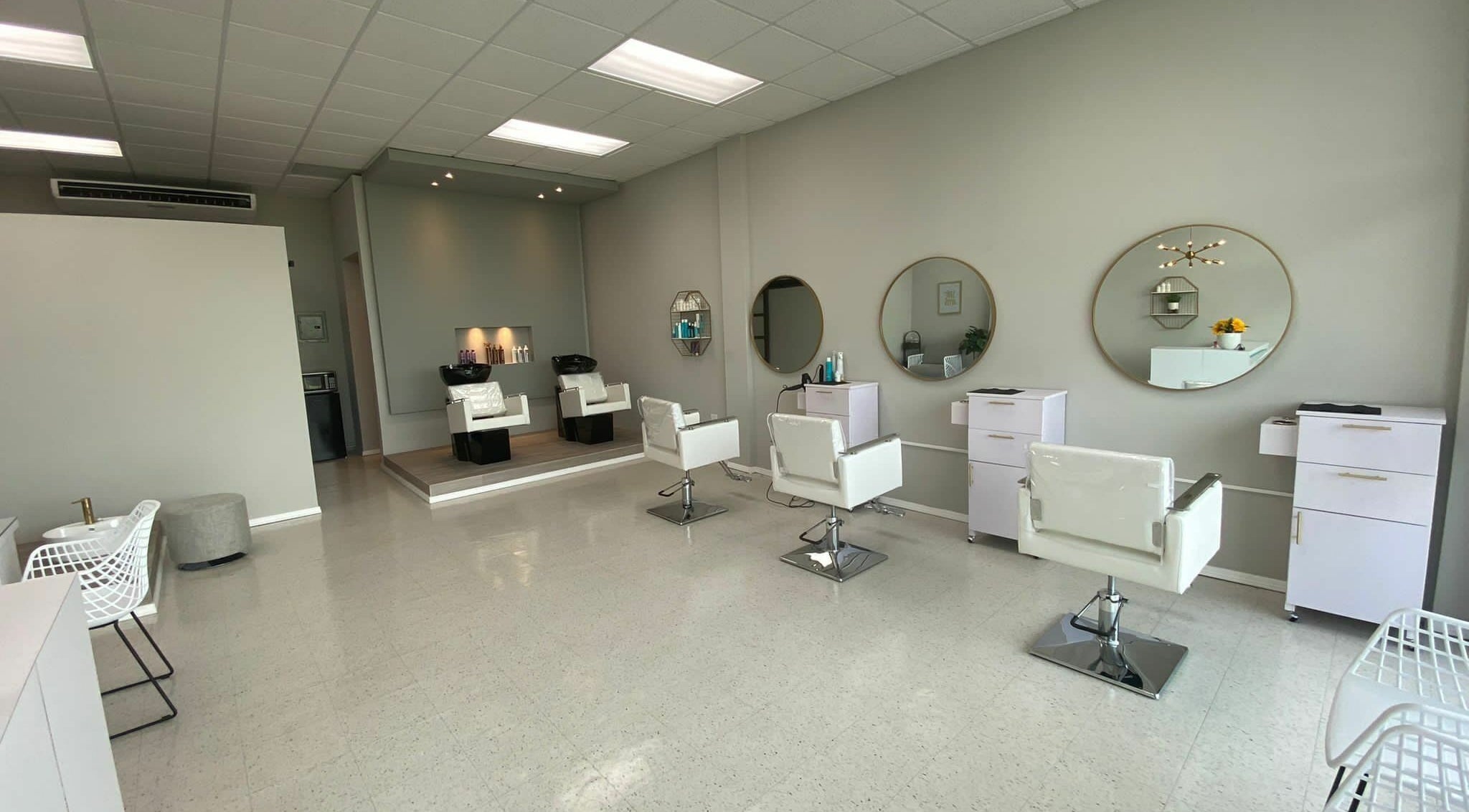 Interior moderno del Adara Hair Salón en Barceloneta, Barceloneta, PR, con sillas blancas y espejos circulares.