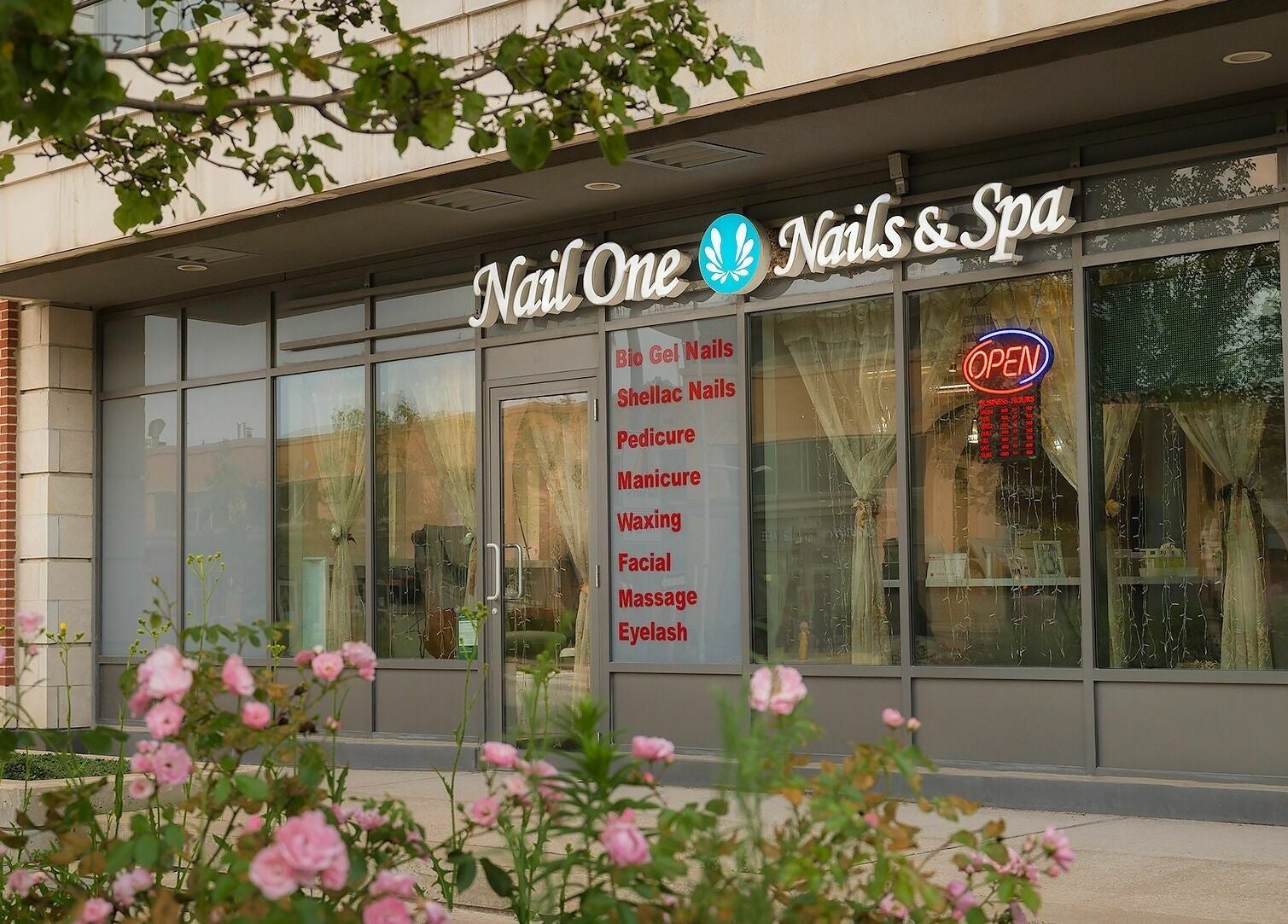 Exterior of Nail One & Spa, Markham, Ontario, CA featuring vibrant signage and pink flowers.