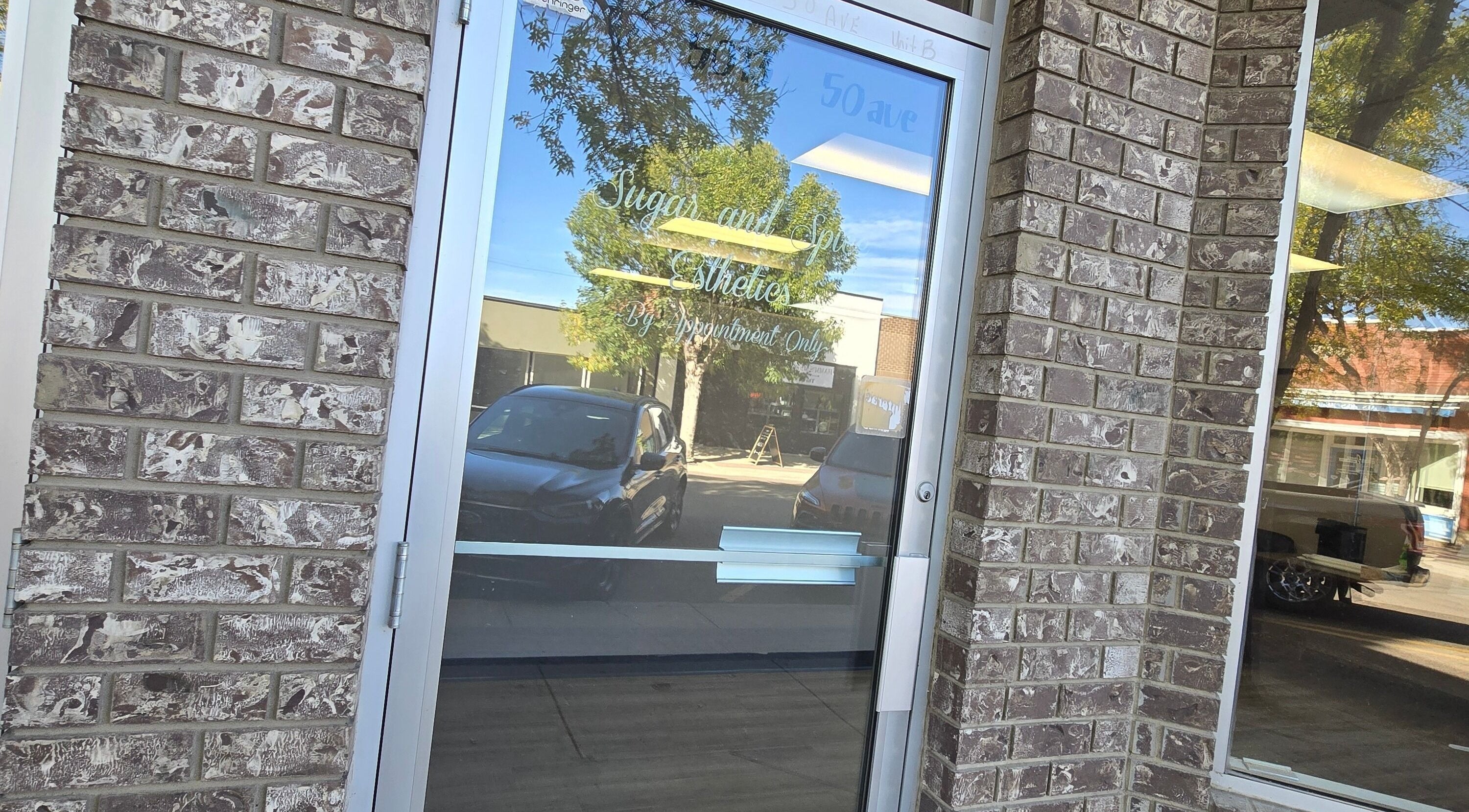 Entrance to Sugar and Spice Esthetics in Ponoka, Alberta, CA showing a glass door with reflection.