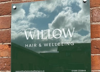 Willow Hair and Wellbeing sign on brick wall, Woodbury, England, GB.
