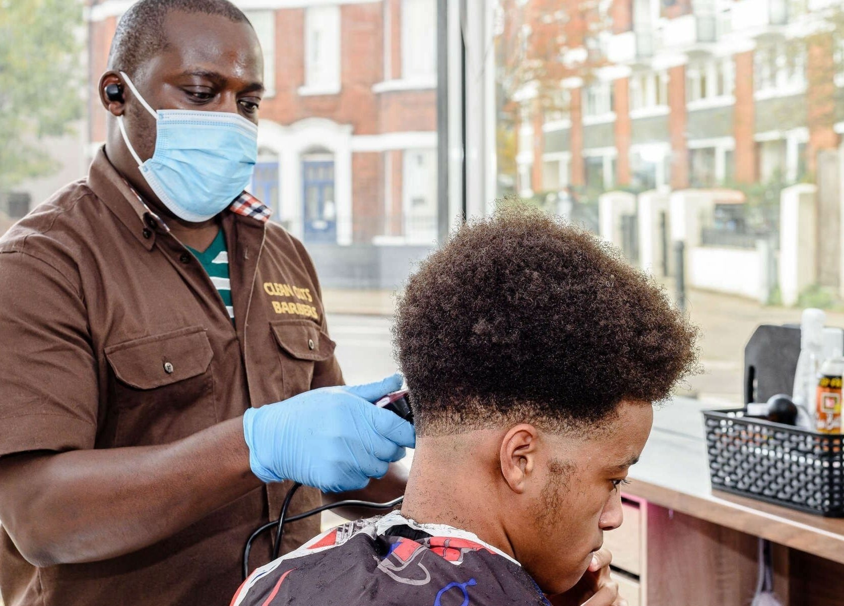 Barber in mask and gloves styling hair at Clean Cuts London, located in London, England, GB.