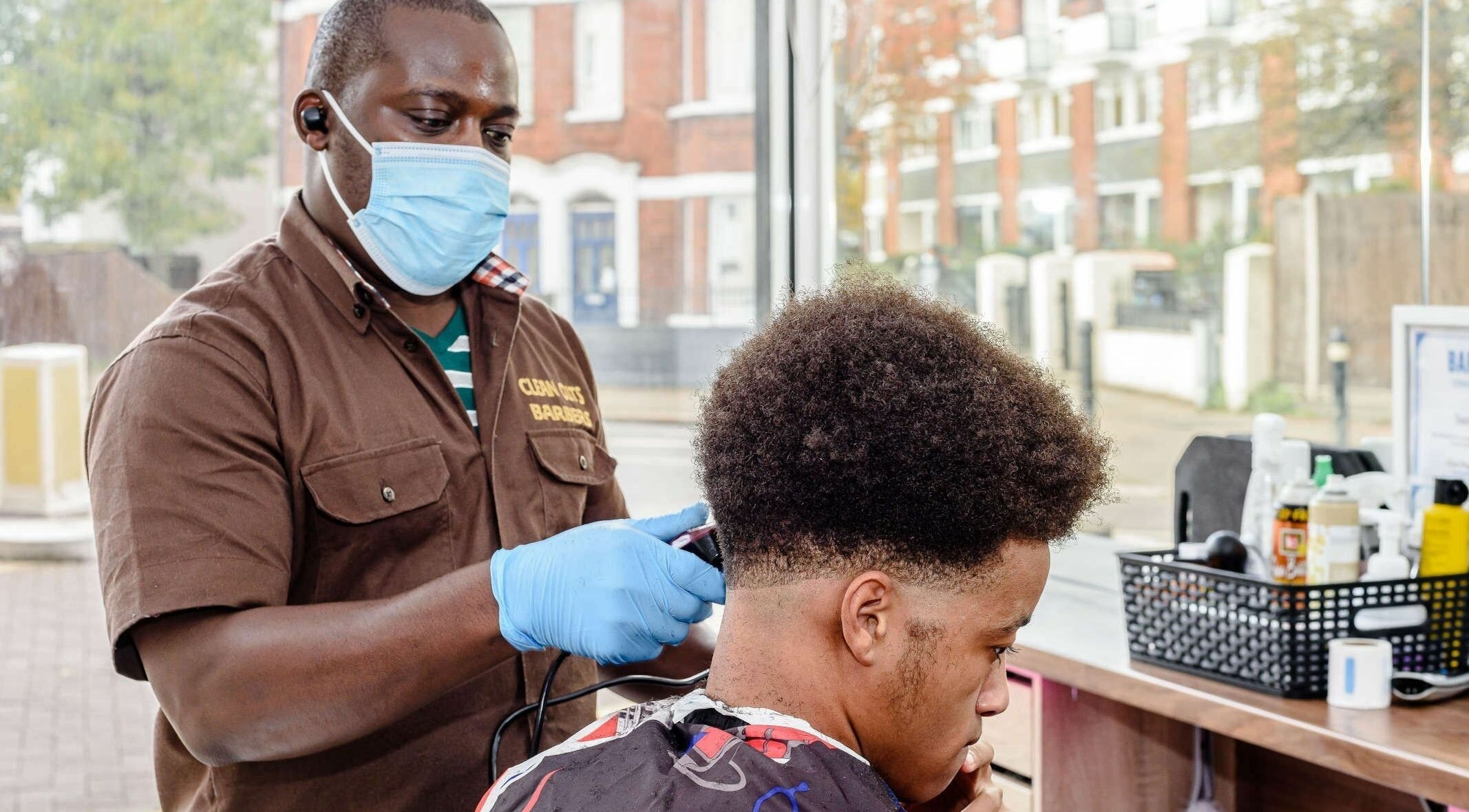 Barber in mask and gloves styling hair at Clean Cuts London, located in London, England, GB.
