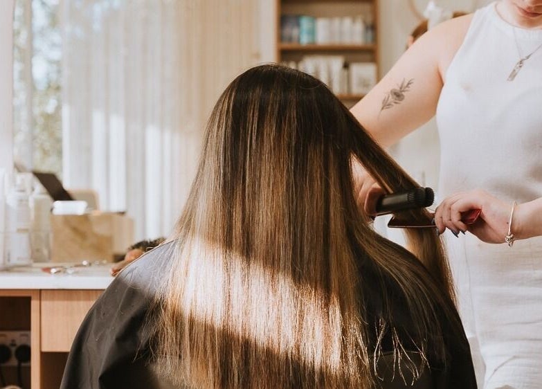 Hair stylist straightens client's hair at Beauty and The Fox in Merewether, New South Wales, AU.