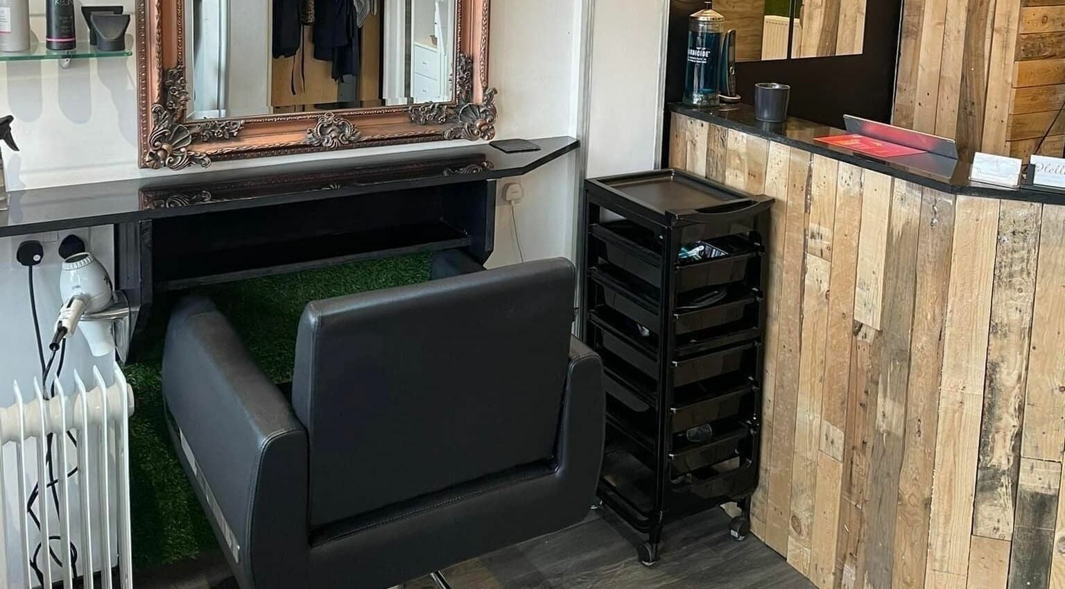 Modern salon station at Platform 169, Exeter, England, GB. Features styling chair, mirror, and wooden decor.