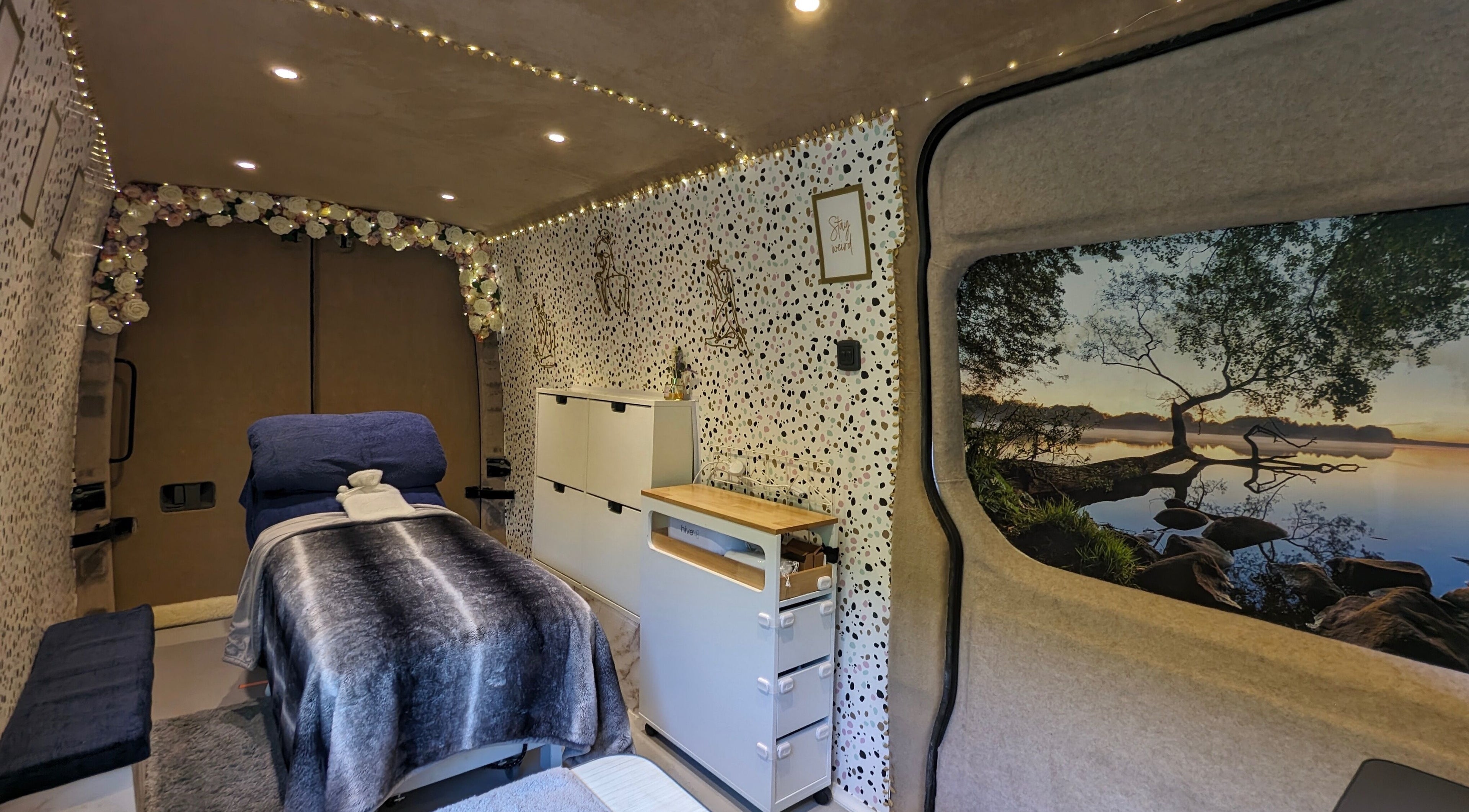 Inside The Beauty Bus in Oxfordshire, GB, showcasing a serene setup with cozy lighting and a massage bed.