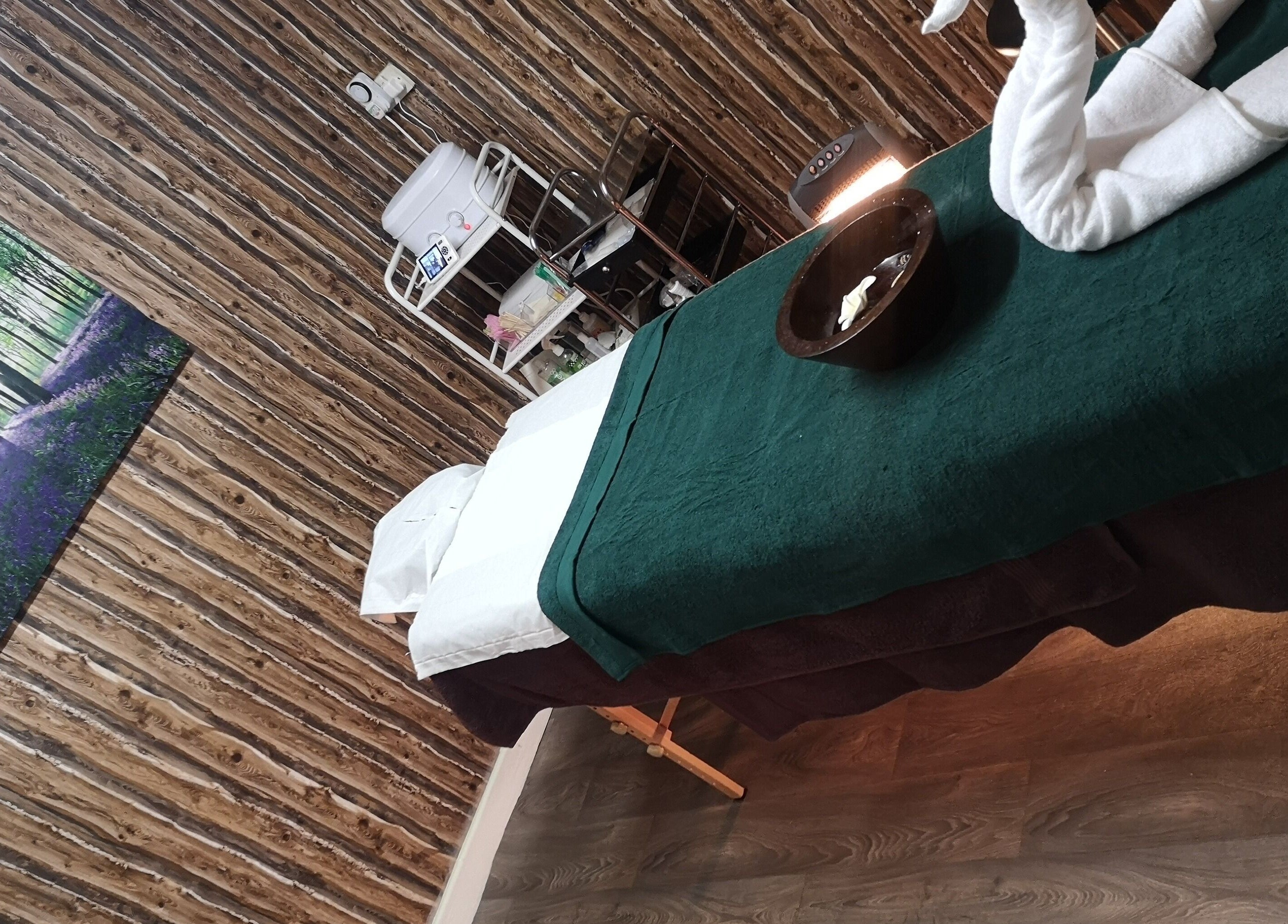 Cozy massage room at Pampered Retreat, Bangor, Wales, GB with a green covered table and wooden decor.
