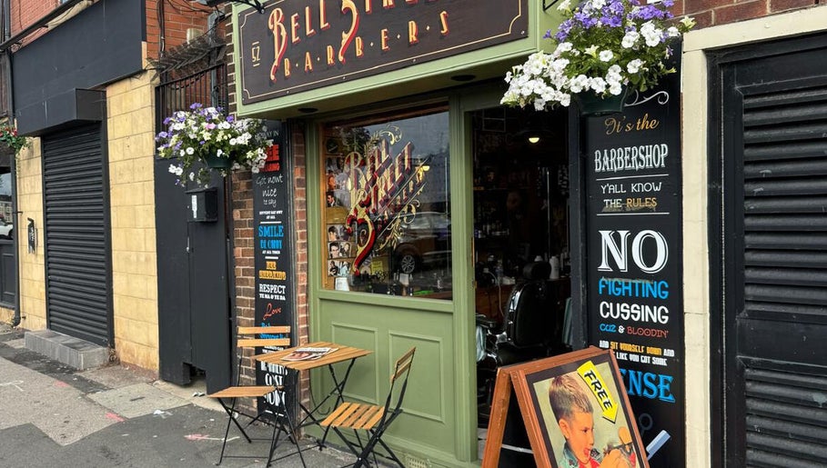 Charming exterior of Bell St. Barbers in North Shields, England, GB adorned with flowers and vintage signs.