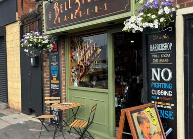 Charming exterior of Bell St. Barbers in North Shields, England, GB adorned with flowers and vintage signs.