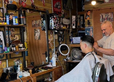 Interior of Bell St. Barbers, North Shields, England, GB showing a barber styling a client's hair.