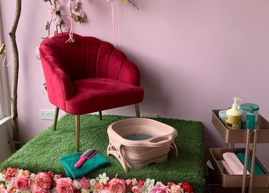 Cozy pedicure area with red chair at Hello Beautiful, Lytham, England, GB framed by flowers and soft lighting.