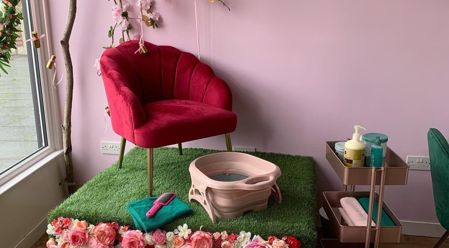 Cozy pedicure area with red chair at Hello Beautiful, Lytham, England, GB framed by flowers and soft lighting.
