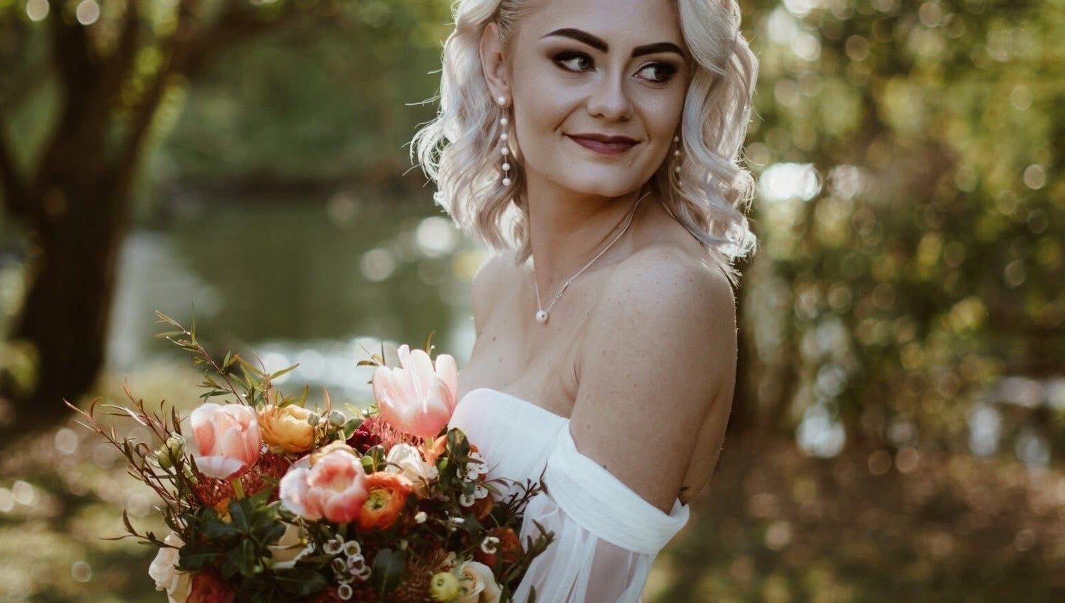 A smiling bride with a bouquet at Skoonveldt, Klerksdorp, North West, ZA, surrounded by lush greenery.