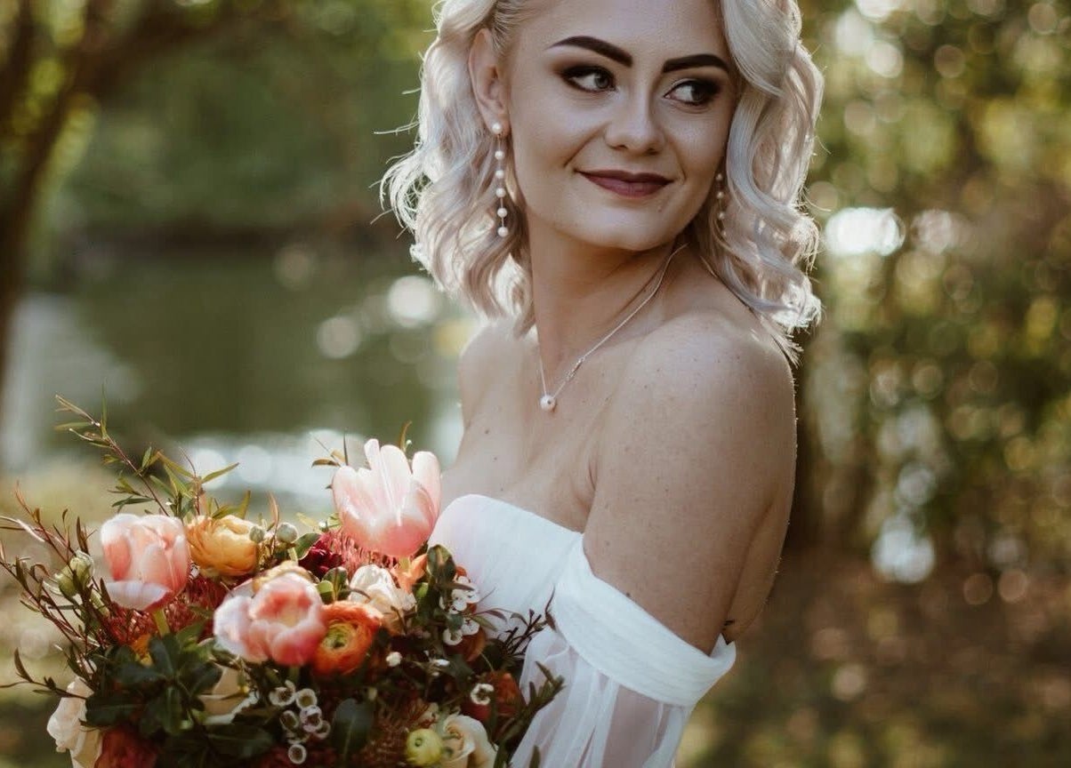 A smiling bride with a bouquet at Skoonveldt, Klerksdorp, North West, ZA, surrounded by lush greenery.