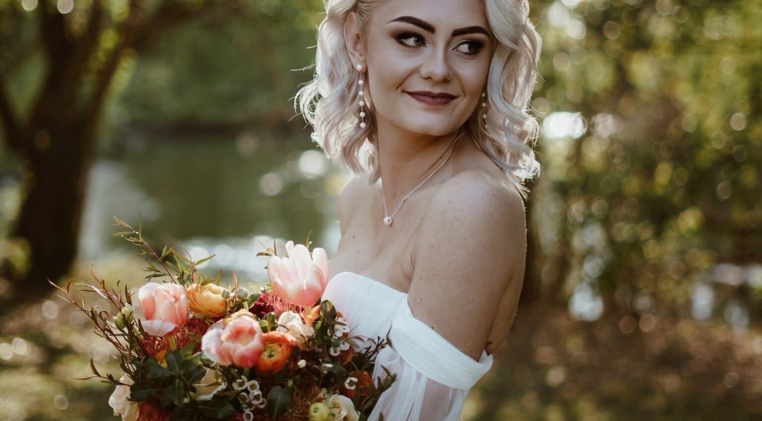 A smiling bride with a bouquet at Skoonveldt, Klerksdorp, North West, ZA, surrounded by lush greenery.