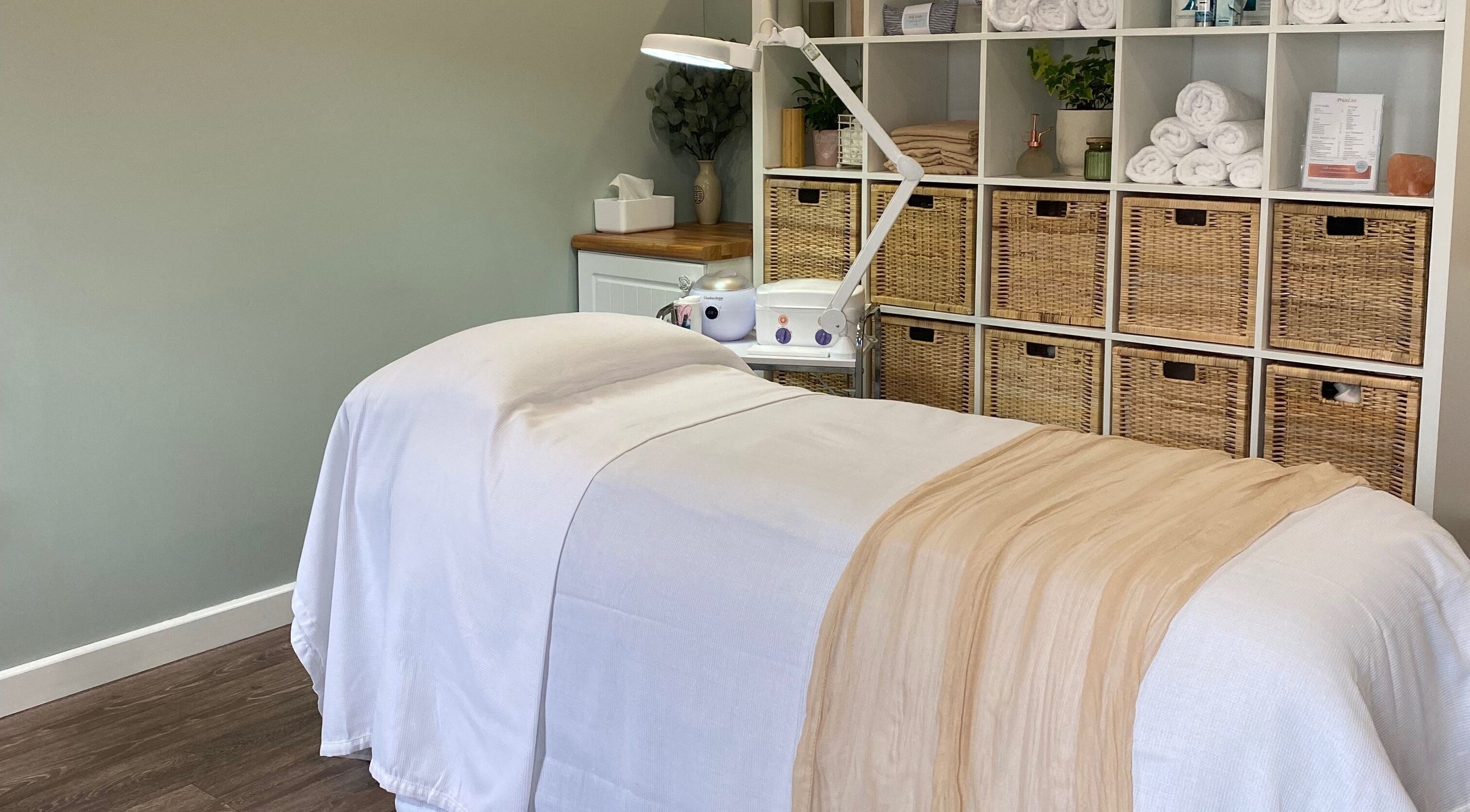 Tranquil treatment room at Primrose Beauty, Yaxley, England, GB with massage table and shelves of towels.