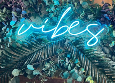 Neon 'vibes' sign amidst lush greenery at Nv Studio, Exeter, England, GB.