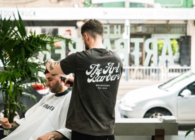 Barber styling a man's hair at The Art Barbers Malvern, Melbourne, Victoria, AU with greenery in background.